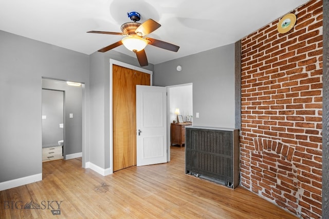 unfurnished bedroom featuring light hardwood / wood-style flooring, a closet, ceiling fan, and brick wall