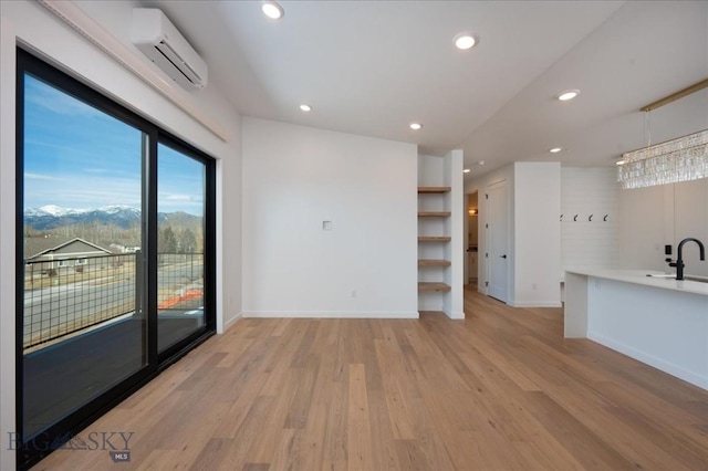 unfurnished living room featuring sink, light wood-type flooring, and an AC wall unit