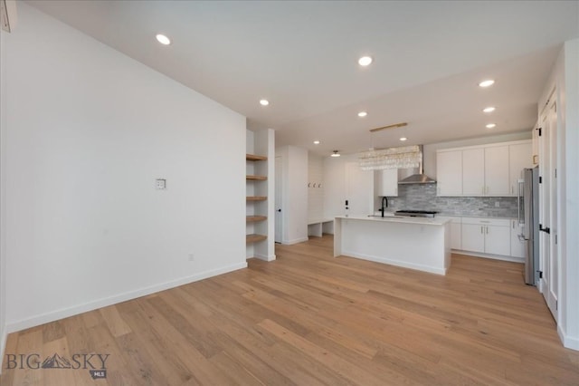 kitchen with sink, stainless steel refrigerator, white cabinetry, a center island with sink, and wall chimney exhaust hood