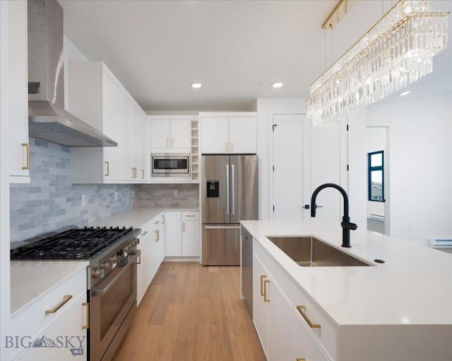 kitchen with sink, appliances with stainless steel finishes, an island with sink, decorative light fixtures, and wall chimney exhaust hood