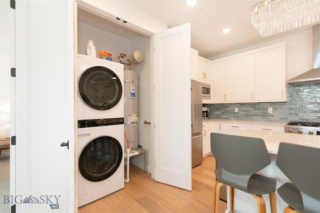 laundry area with stacked washer / drying machine, water heater, and light hardwood / wood-style flooring