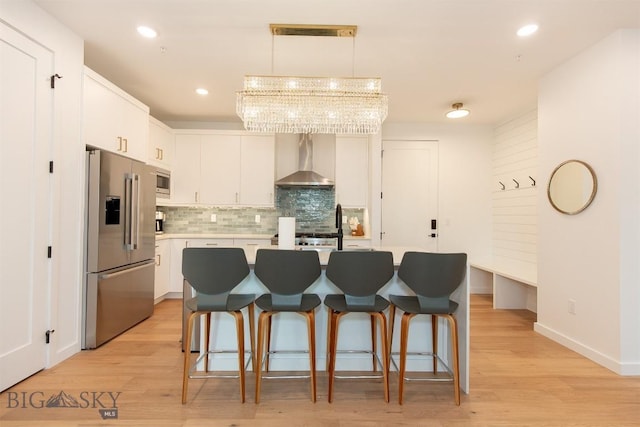 kitchen featuring appliances with stainless steel finishes, white cabinetry, hanging light fixtures, a center island, and wall chimney exhaust hood