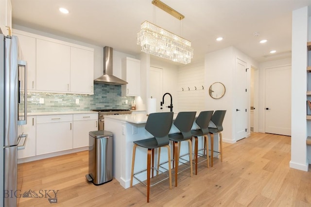 kitchen with a center island with sink, wall chimney range hood, pendant lighting, stainless steel appliances, and white cabinets