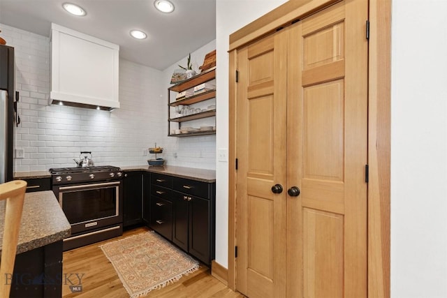 kitchen with light hardwood / wood-style floors, custom exhaust hood, gas range, and tasteful backsplash