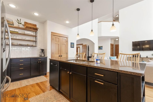 kitchen featuring appliances with stainless steel finishes, decorative light fixtures, light hardwood / wood-style floors, and an island with sink