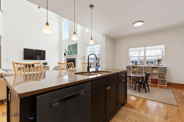 kitchen featuring sink, dishwasher, decorative light fixtures, an island with sink, and light stone countertops