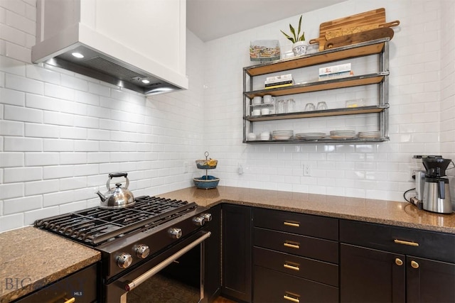 kitchen with wall chimney exhaust hood, light stone counters, backsplash, and stainless steel gas range oven