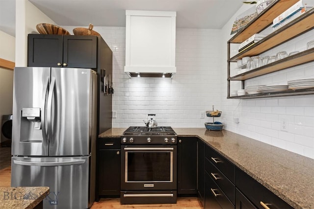 kitchen with stainless steel fridge with ice dispenser, range with gas stovetop, tasteful backsplash, custom range hood, and dark stone countertops