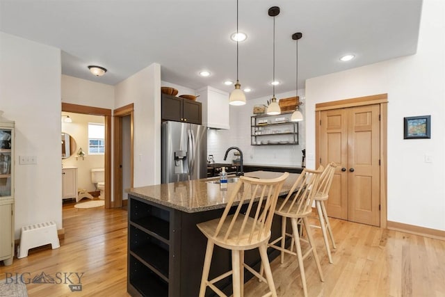 kitchen with a center island with sink, sink, pendant lighting, a kitchen breakfast bar, and stainless steel fridge