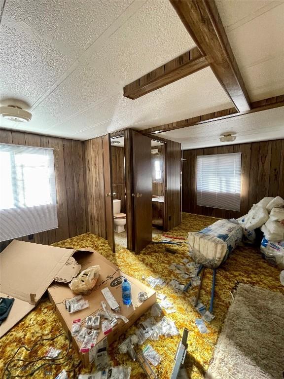 bedroom with a textured ceiling, carpet, connected bathroom, and wooden walls