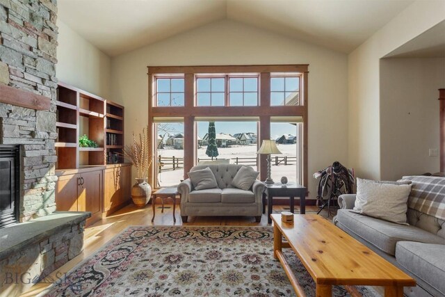 living room with high vaulted ceiling, a healthy amount of sunlight, a stone fireplace, and light wood-type flooring