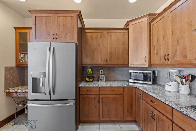 kitchen with stainless steel appliances, light tile patterned floors, backsplash, and light stone counters