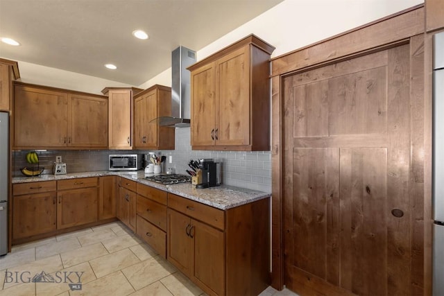 kitchen featuring wall chimney range hood, decorative backsplash, stainless steel appliances, and light stone countertops
