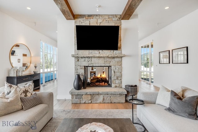 living room with beam ceiling, a stone fireplace, and hardwood / wood-style flooring