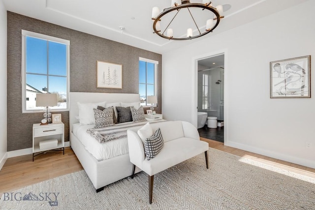 bedroom with multiple windows, light hardwood / wood-style flooring, connected bathroom, and a notable chandelier