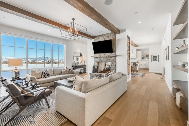 living room with light hardwood / wood-style floors, beamed ceiling, an inviting chandelier, and a stone fireplace