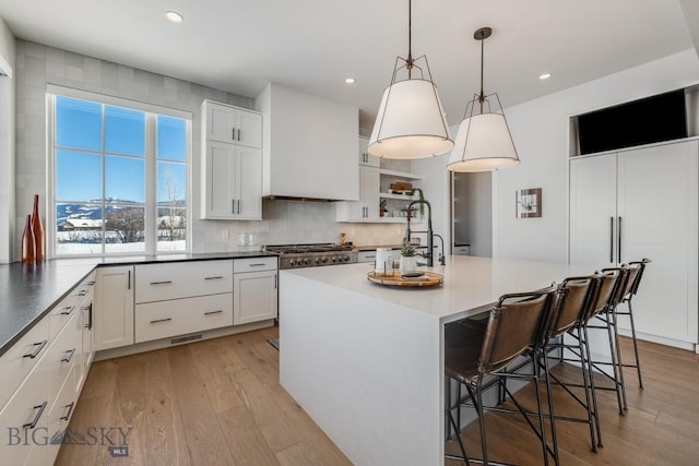 kitchen featuring an island with sink, a kitchen bar, white cabinetry, and decorative light fixtures