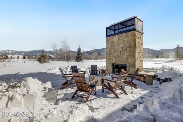 snow covered patio with a mountain view and an outdoor stone fireplace