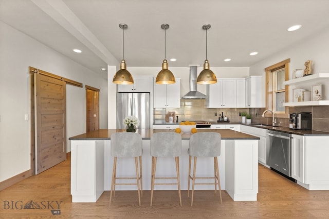 kitchen with stainless steel appliances, a kitchen island, sink, white cabinets, and wall chimney range hood