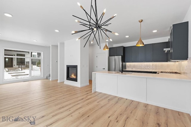 kitchen featuring appliances with stainless steel finishes, light wood-type flooring, pendant lighting, kitchen peninsula, and tasteful backsplash