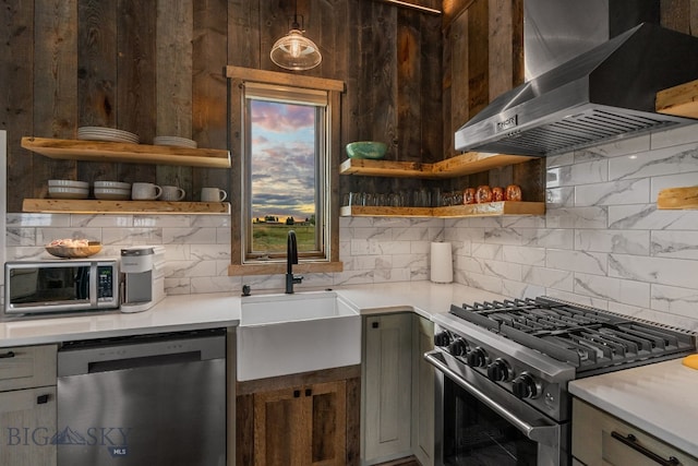 kitchen with appliances with stainless steel finishes, tasteful backsplash, wall chimney range hood, pendant lighting, and sink