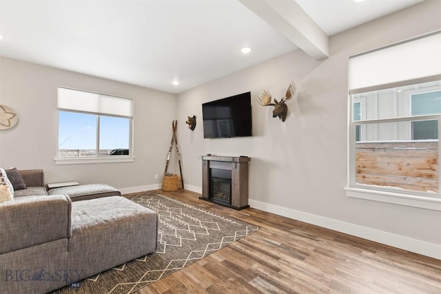 living room with recessed lighting, a glass covered fireplace, wood finished floors, beamed ceiling, and baseboards