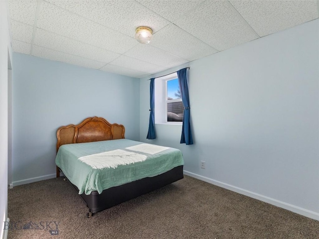 carpeted bedroom featuring a drop ceiling and baseboards