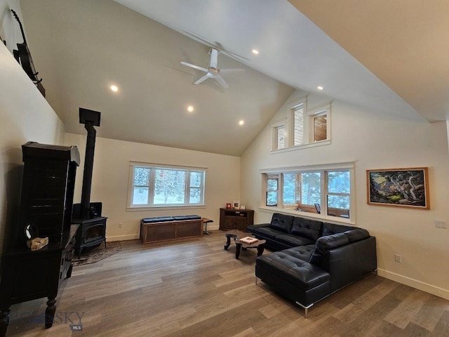 living area with a wood stove, baseboards, high vaulted ceiling, and wood finished floors