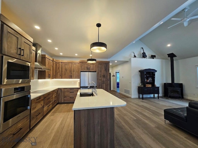 kitchen featuring open floor plan, stainless steel appliances, light countertops, wall chimney range hood, and a sink