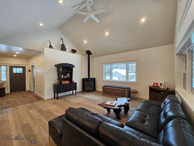 living area with high vaulted ceiling, light wood-style flooring, recessed lighting, baseboards, and a wood stove