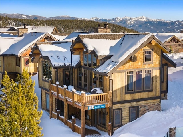 snow covered back of property with a chimney and a mountain view