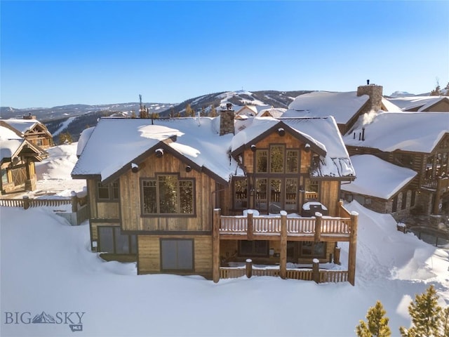 snow covered back of property featuring a mountain view and a chimney