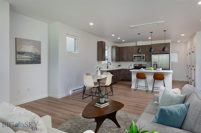 living area featuring light wood finished floors, baseboard heating, recessed lighting, and baseboards