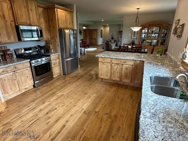 kitchen featuring decorative light fixtures, light wood finished floors, appliances with stainless steel finishes, a sink, and light stone countertops