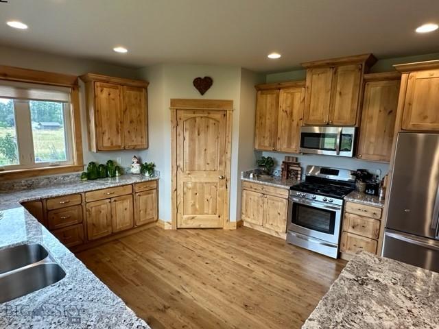 kitchen with light wood-type flooring, light stone countertops, appliances with stainless steel finishes, and recessed lighting