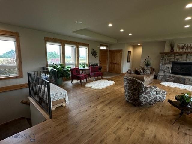 living area featuring a tray ceiling, a stone fireplace, recessed lighting, and wood finished floors