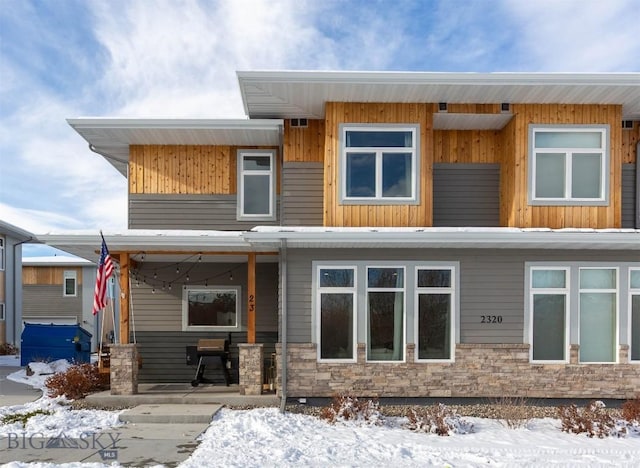 snow covered back of property with stone siding