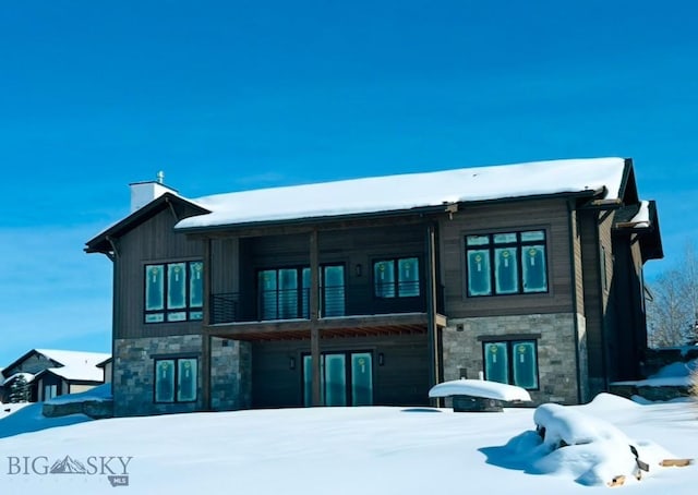 snow covered house with stone siding and a chimney