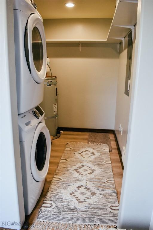 laundry room featuring stacked washer / drying machine, strapped water heater, light wood-style flooring, and laundry area