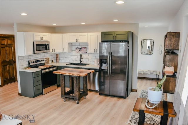 kitchen with light wood finished floors, stainless steel appliances, light countertops, white cabinetry, and a sink