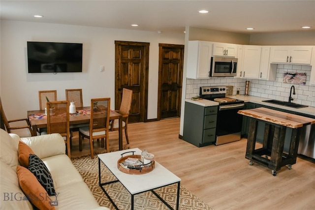 kitchen with a sink, white cabinetry, light wood-style floors, light countertops, and appliances with stainless steel finishes