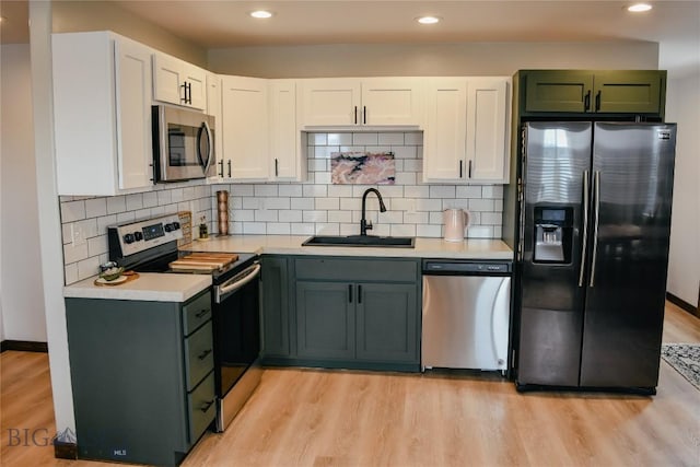 kitchen with stainless steel appliances, a sink, white cabinets, light countertops, and light wood finished floors