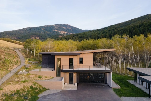 exterior space with aphalt driveway, an attached garage, a wooded view, and a mountain view