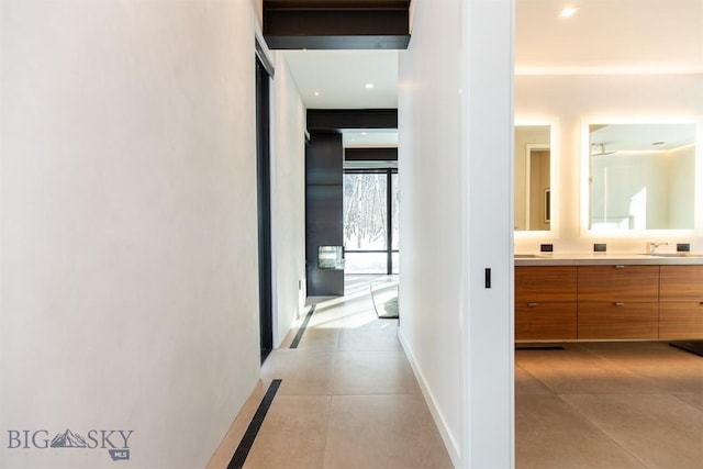 corridor featuring light tile patterned floors, a sink, and baseboards