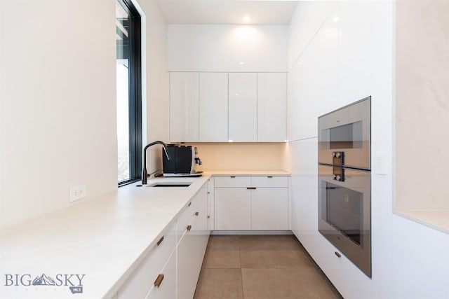 kitchen featuring light tile patterned floors, a sink, white cabinets, light countertops, and modern cabinets