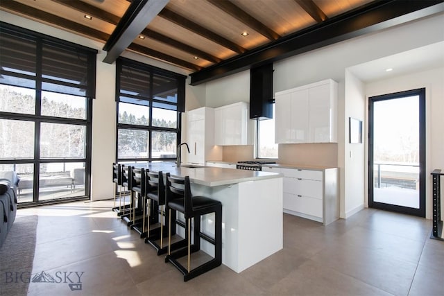 kitchen featuring an island with sink, a breakfast bar area, white cabinets, and beamed ceiling