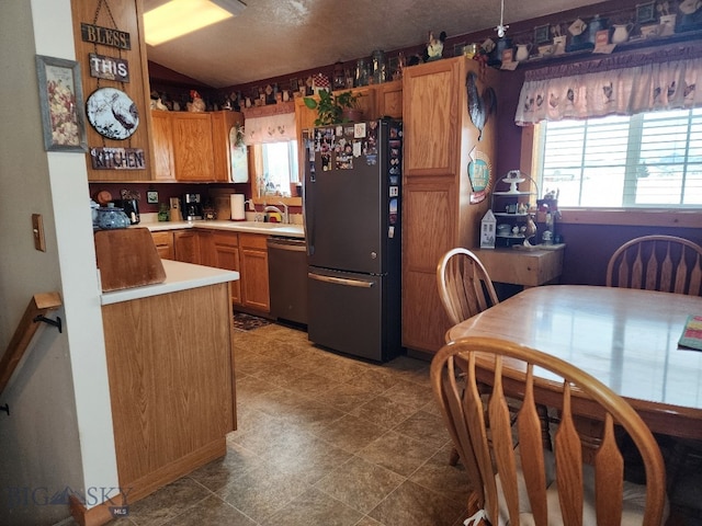 kitchen featuring lofted ceiling, a sink, light countertops, stainless steel dishwasher, and freestanding refrigerator