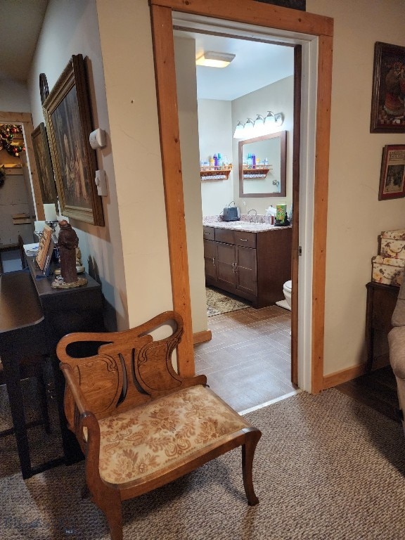 hallway with baseboards, a sink, and light colored carpet