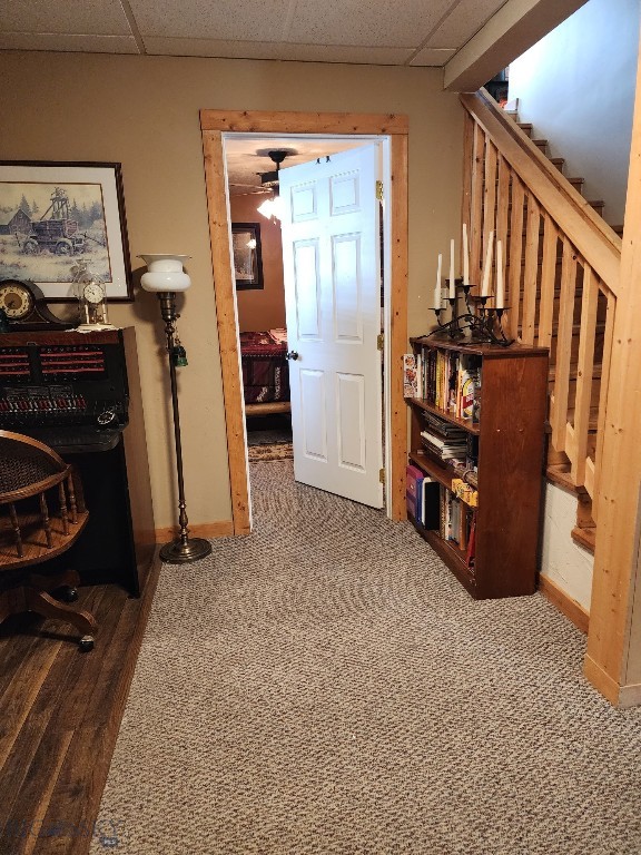 hallway with dark colored carpet, stairway, a paneled ceiling, and baseboards