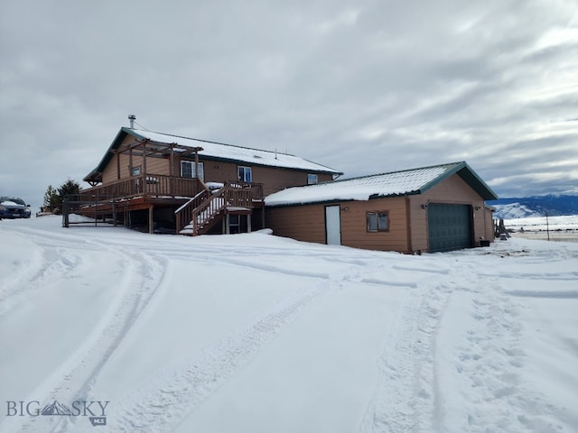 snow covered back of property featuring a garage, a wooden deck, and stairs